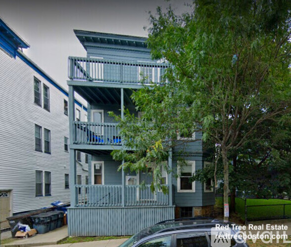 A multi-story building with a balcony and a car parked in front.