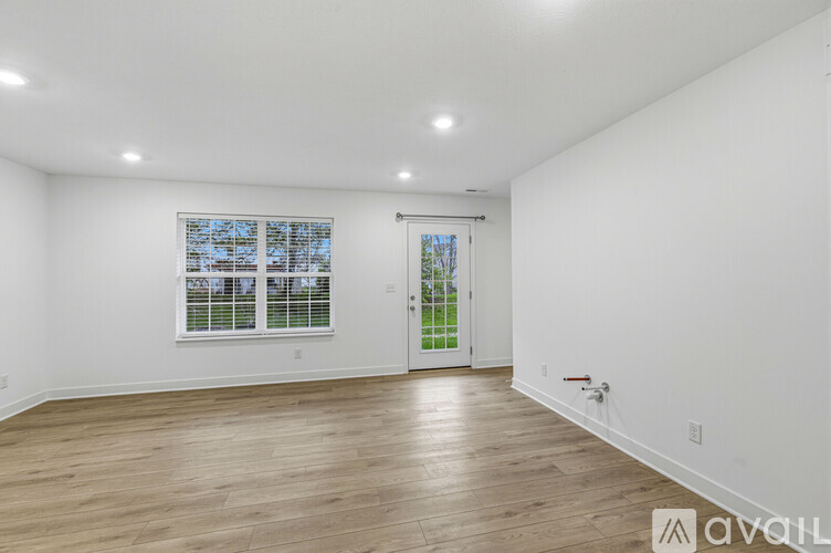 A spacious room with wooden flooring and a large window with blinds.