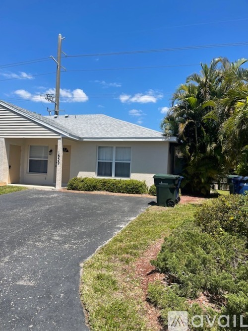 A house with a grey roof and a green trash bin in front.