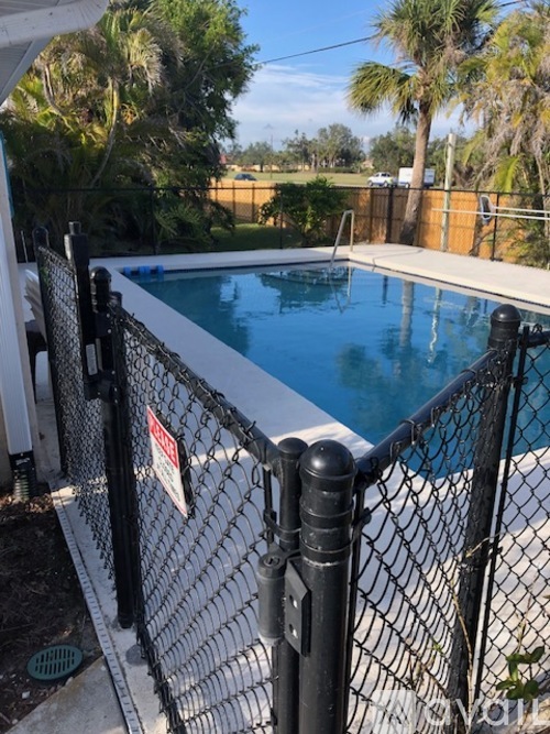 A pool surrounded by a black fence with a sign on it.