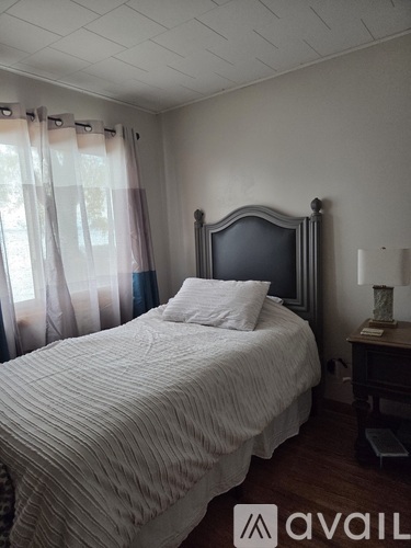A bedroom with a bed, nightstand, and window with curtains.