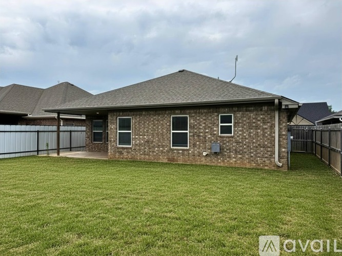 A house with a brown brick exterior and a grey roof is surrounded by a green lawn.