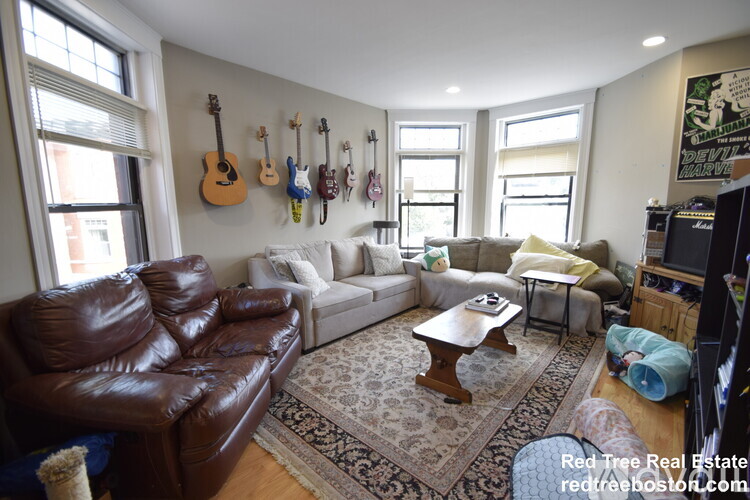 A living room with a brown leather couch and a guitar wall hanging.
