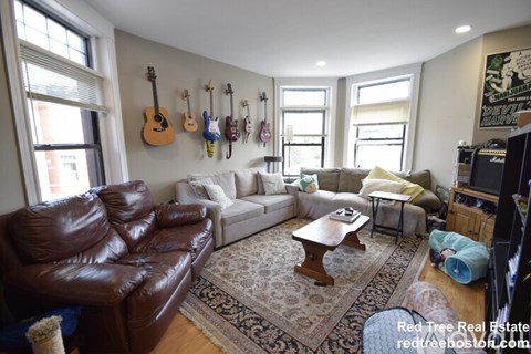 A living room with a brown leather couch and a guitar wall hanging.