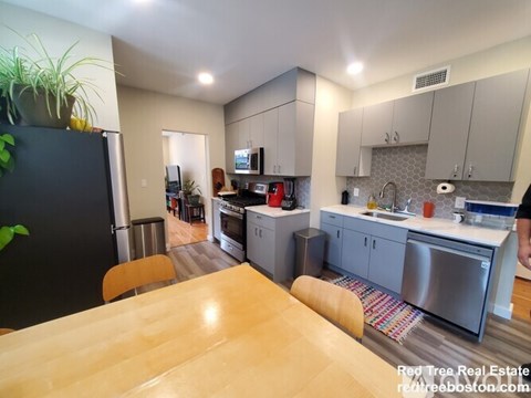 A kitchen with a table in the middle and a refrigerator on the left.