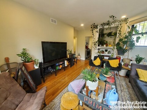 A living room with a brown couch, a TV, and a coffee table with various objects on it.