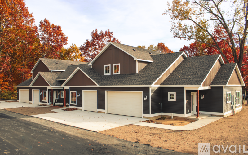 A house with a brown roof and grey walls is surrounded by trees with orange leaves.