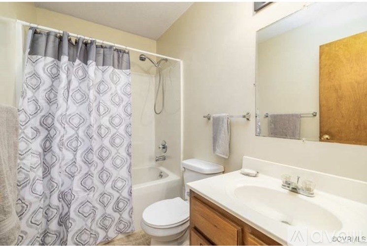 A bathroom with a white toilet, a white sink, a shower curtain, and a wooden cabinet.