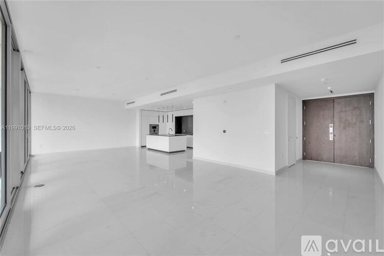 A spacious, empty room with a white floor and walls, and a wooden door on the right side.