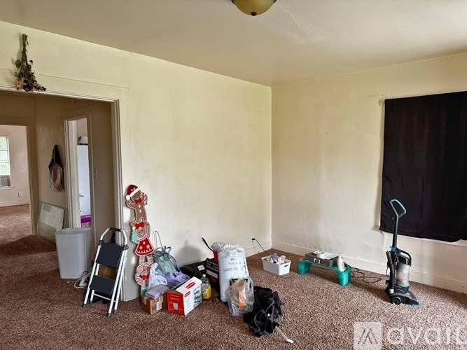 A room with a carpet, a vacuum cleaner, a broom, a box, and a chair.