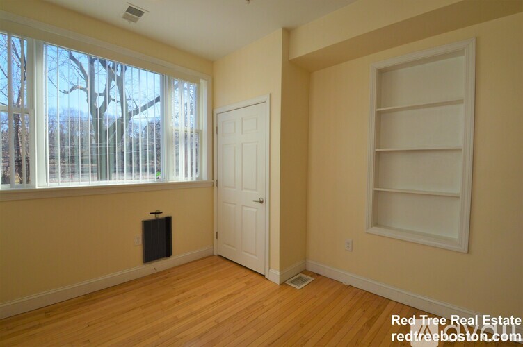 A room with a white door and a window with a view of trees outside.