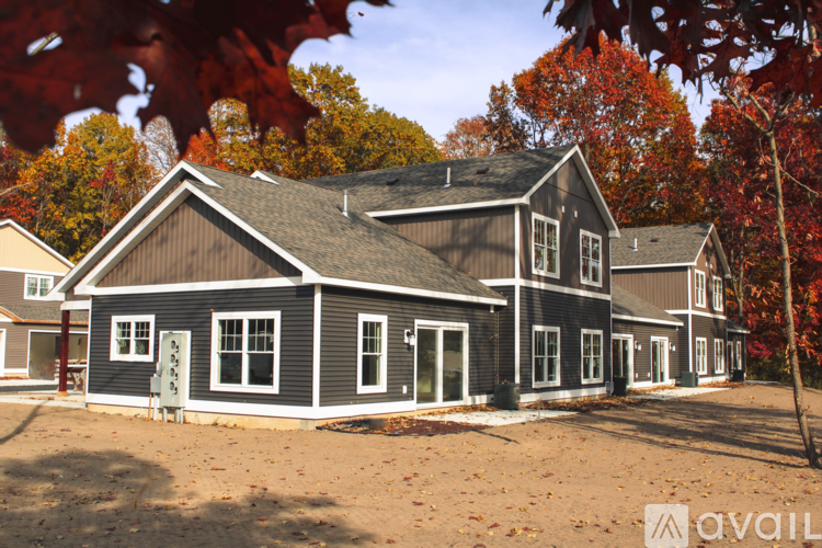 A house with a grey exterior and a brown roof is surrounded by trees with red leaves.