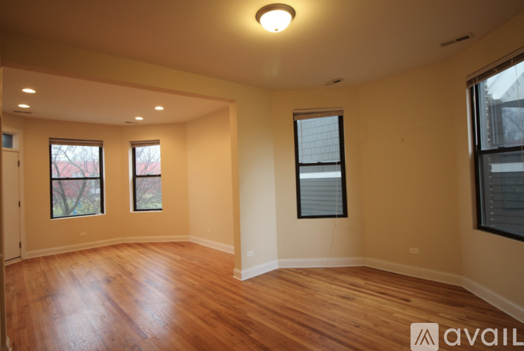 A spacious room with wooden floors and three windows.