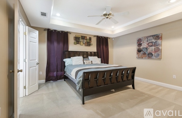 A bedroom with a bed, a ceiling fan, and a painting on the wall.
