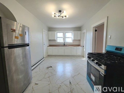 A kitchen with a stainless steel refrigerator, a black stove, and white cabinets.