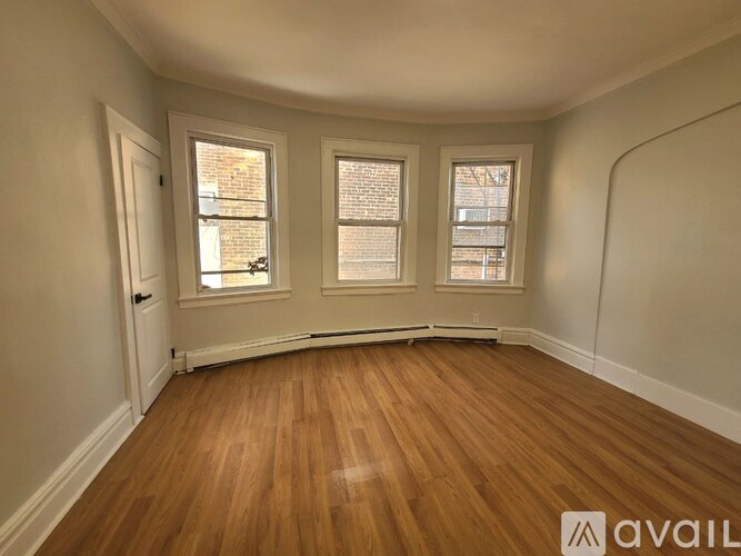 A room with wooden flooring and three windows.