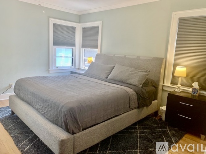 A bedroom with a large bed, a nightstand with a lamp, and a window with blinds.