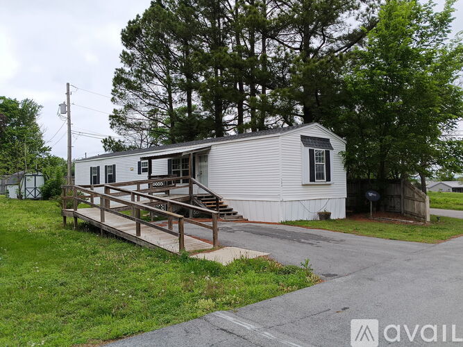 A mobile home with a deck is surrounded by greenery and a cloudy sky.