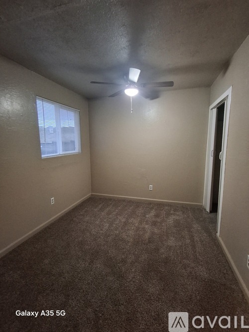 A room with a carpeted floor, a ceiling fan, and a window with blinds.