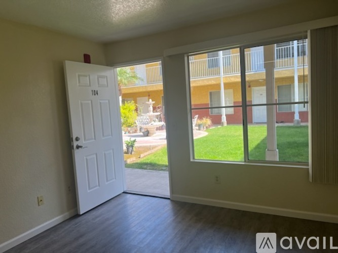 A room with a white door and a window overlooking a balcony with a view of a building and greenery.