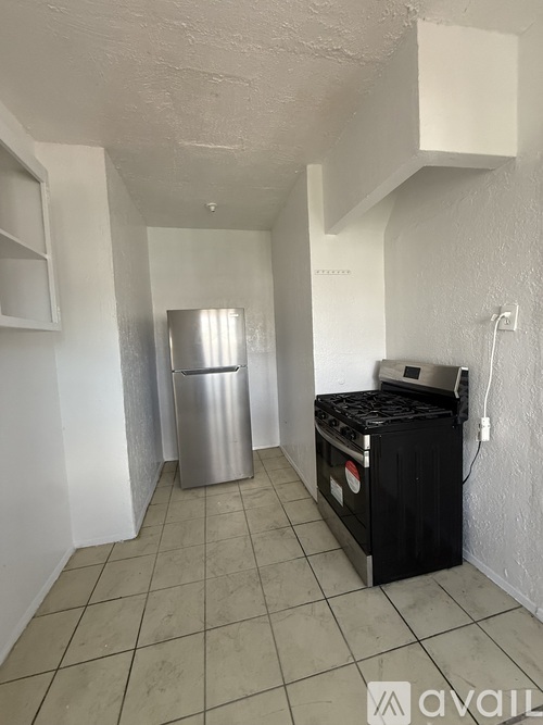 A kitchen area with a stainless steel trash can, a black stove, and a white fridge.