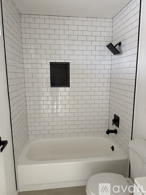 A white tiled bathroom with a white bathtub and toilet.