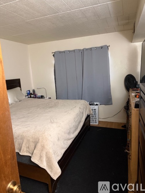 A bedroom with a bed, nightstand, and window with a grey curtain.
