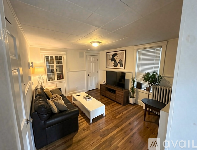 A living room with a black couch, a white coffee table, and a wooden floor.