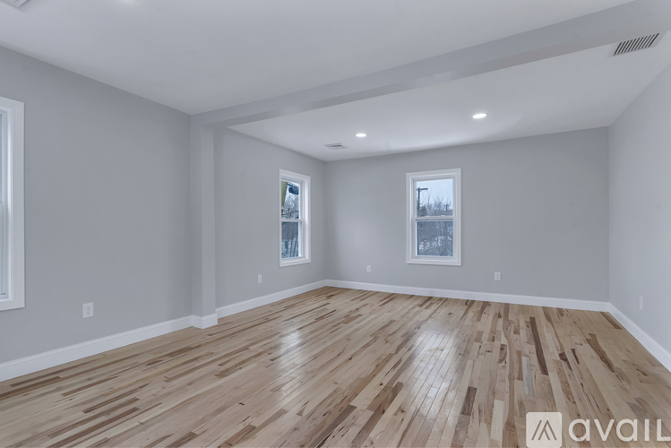 A spacious room with wooden flooring and two windows.