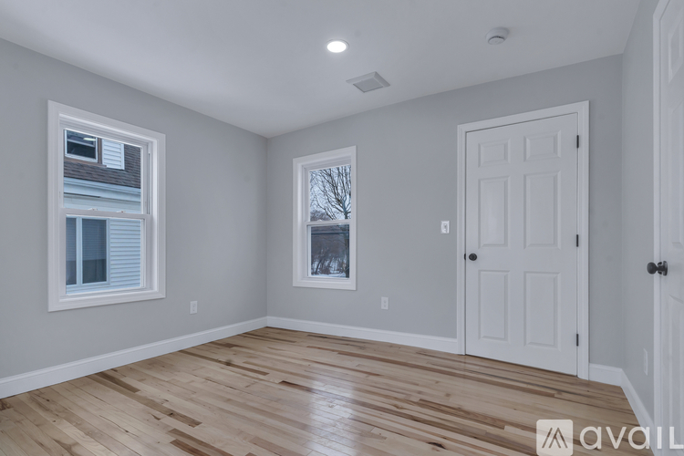 A room with wooden floors and white walls, featuring a window with a view of a house and bare trees outside.