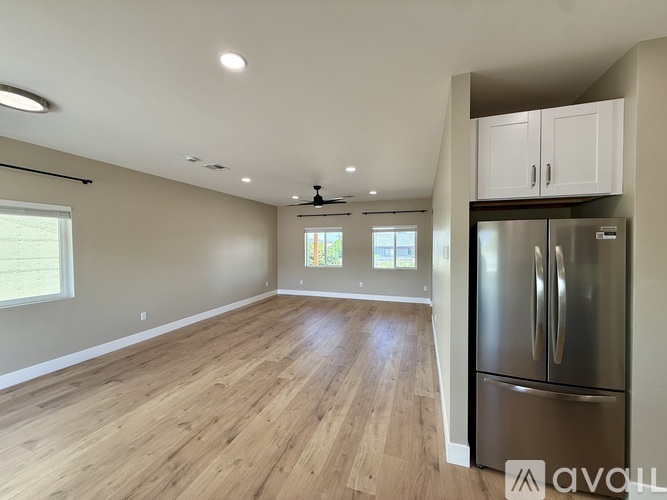 A spacious room with wooden flooring and a stainless steel refrigerator.