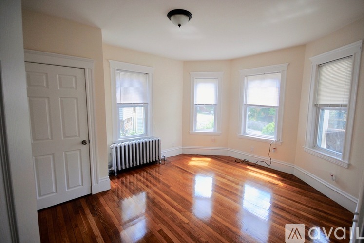 A room with wooden floors and white walls has a door and three windows.