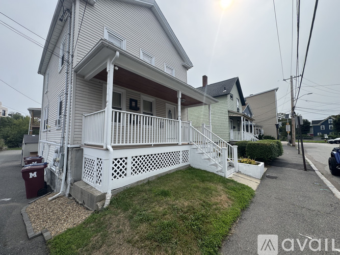 A house with a white porch and a red trash can in front of it.