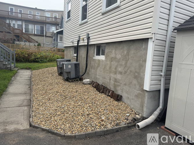 A gravel area in front of a house with a grey wall and a white garage door.