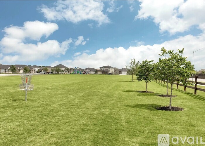 A grassy field with a disc golf basket and trees in the distance.