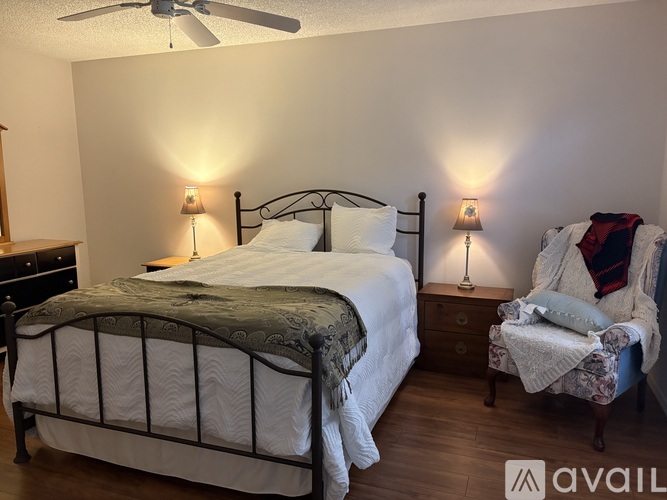 A bedroom with a bed, chair, and two lamps.