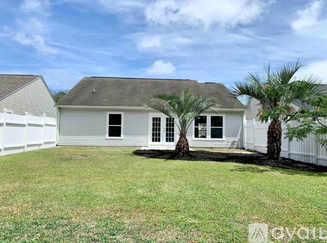 A house with a grey roof and white fence is surrounded by a grassy area.