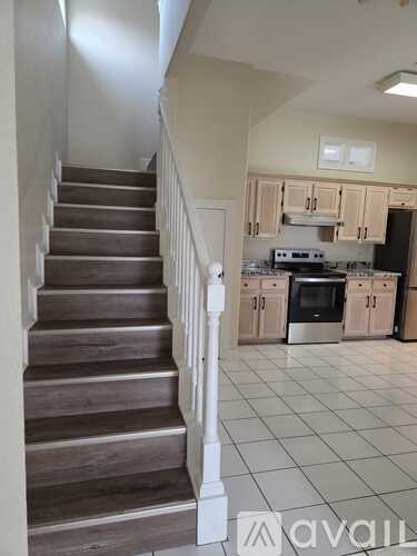 A staircase with a white railing leads to a kitchen.