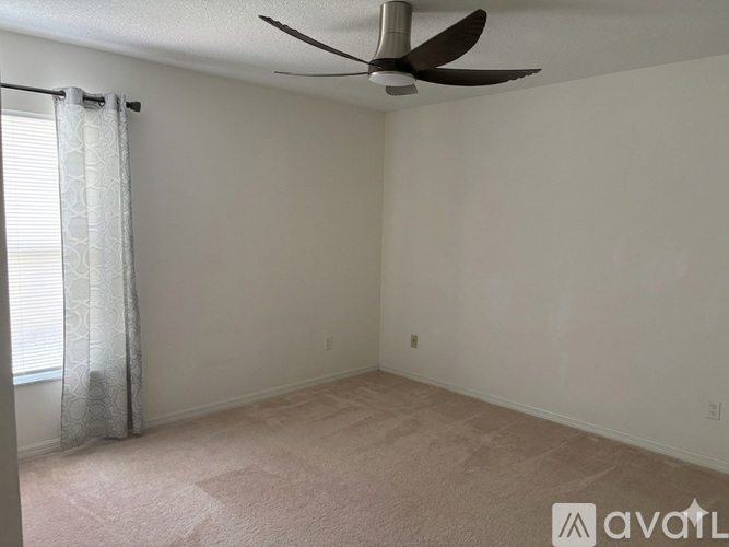 A bedroom with a bed, a ceiling fan, and a window with curtains.
