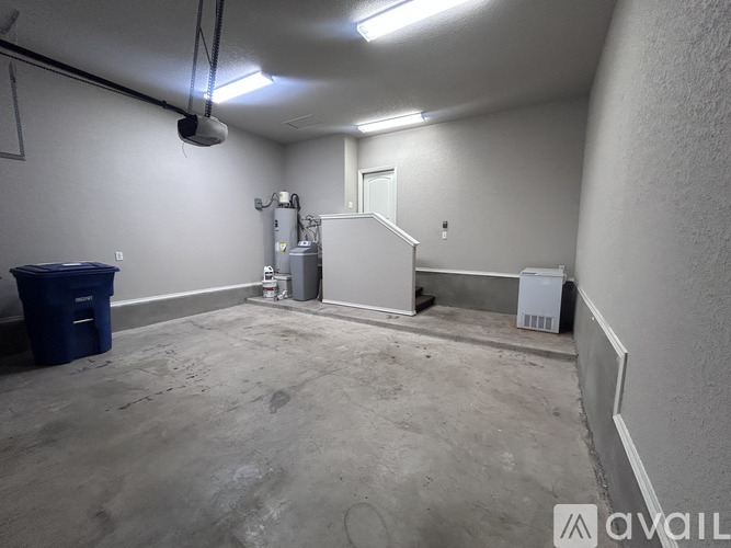 A large empty room with a blue bin and a white door.