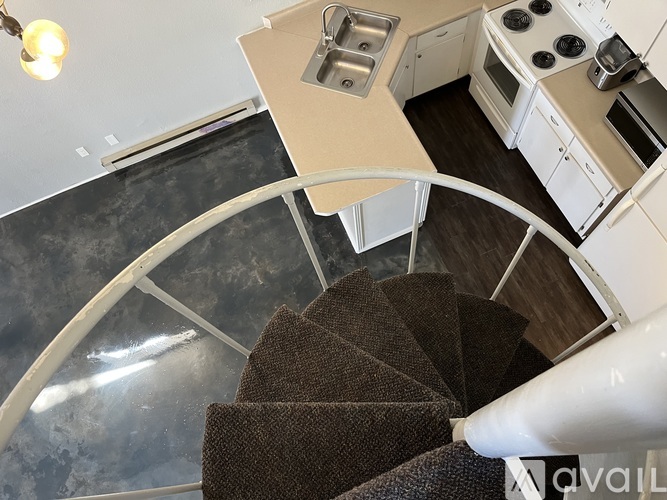 A spiral staircase with a brown carpeted runner leads to a kitchen.