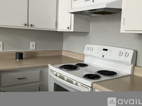 A white stove top oven with four burners is in a kitchen with white cabinets.