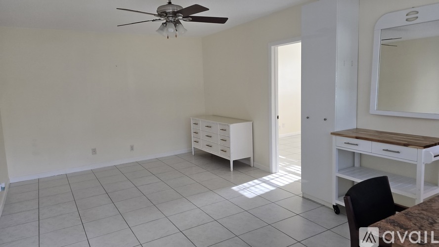 A room with a ceiling fan, a desk with a chair, and a large mirror.