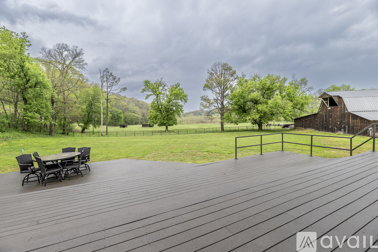 A wooden deck with a table and chairs overlooks a grassy field and a barn.