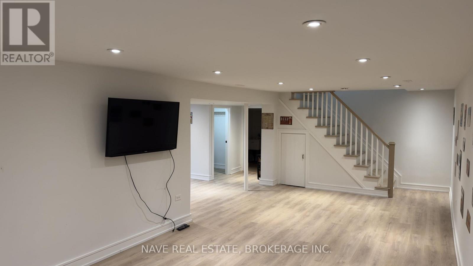 A spacious room with a staircase and a flat screen TV mounted on the wall.