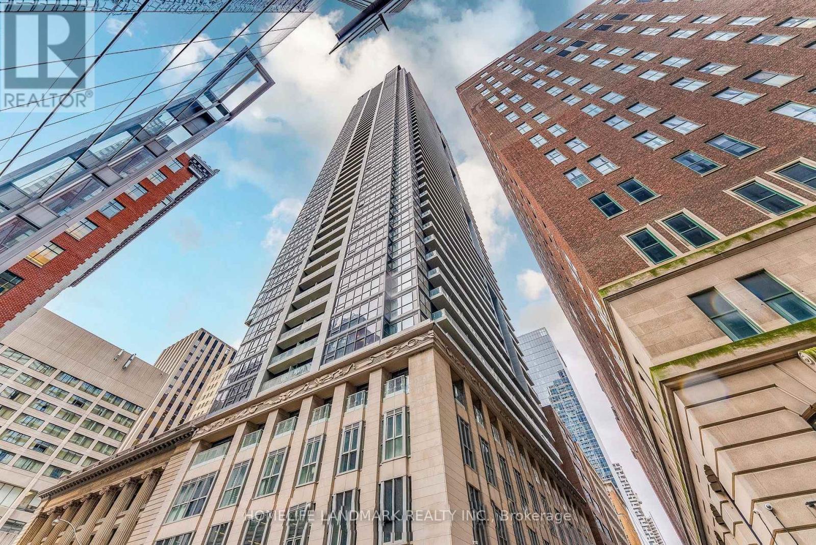 A tall building with a glass facade stands in front of other buildings.