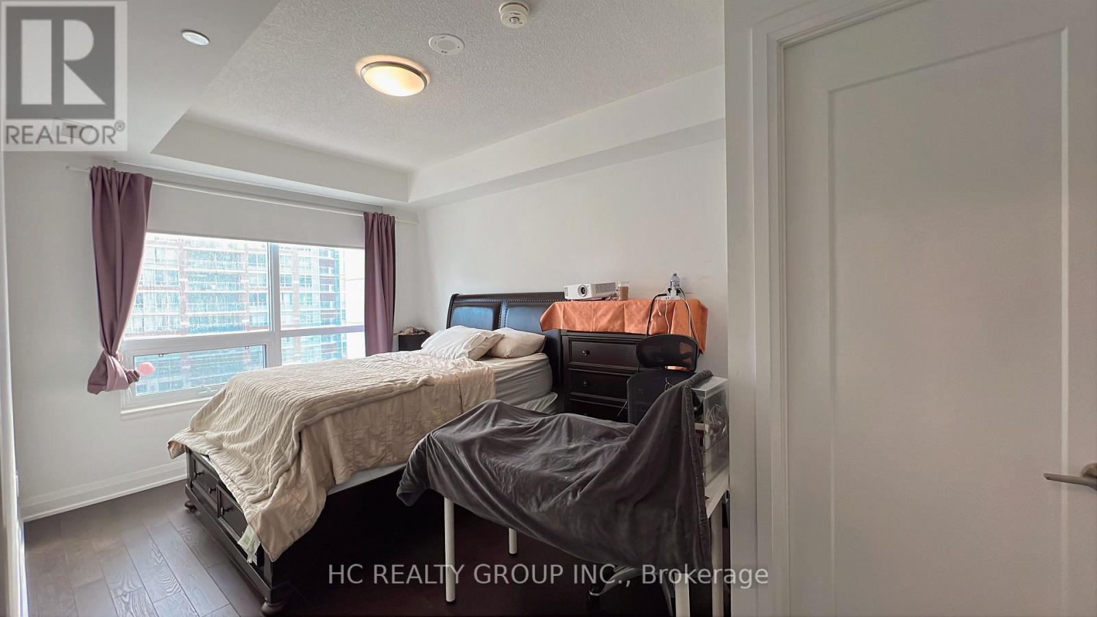 A bedroom with a bed, a desk with a printer, and a window with curtains.