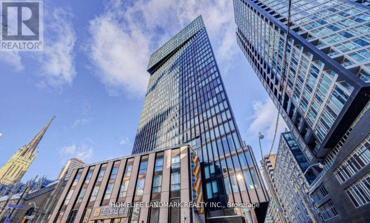 A tall building with a glass facade stands in front of a skyline of other buildings.