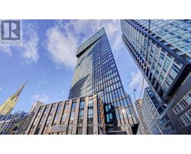 A tall building with a glass facade stands in front of a skyline of other buildings.