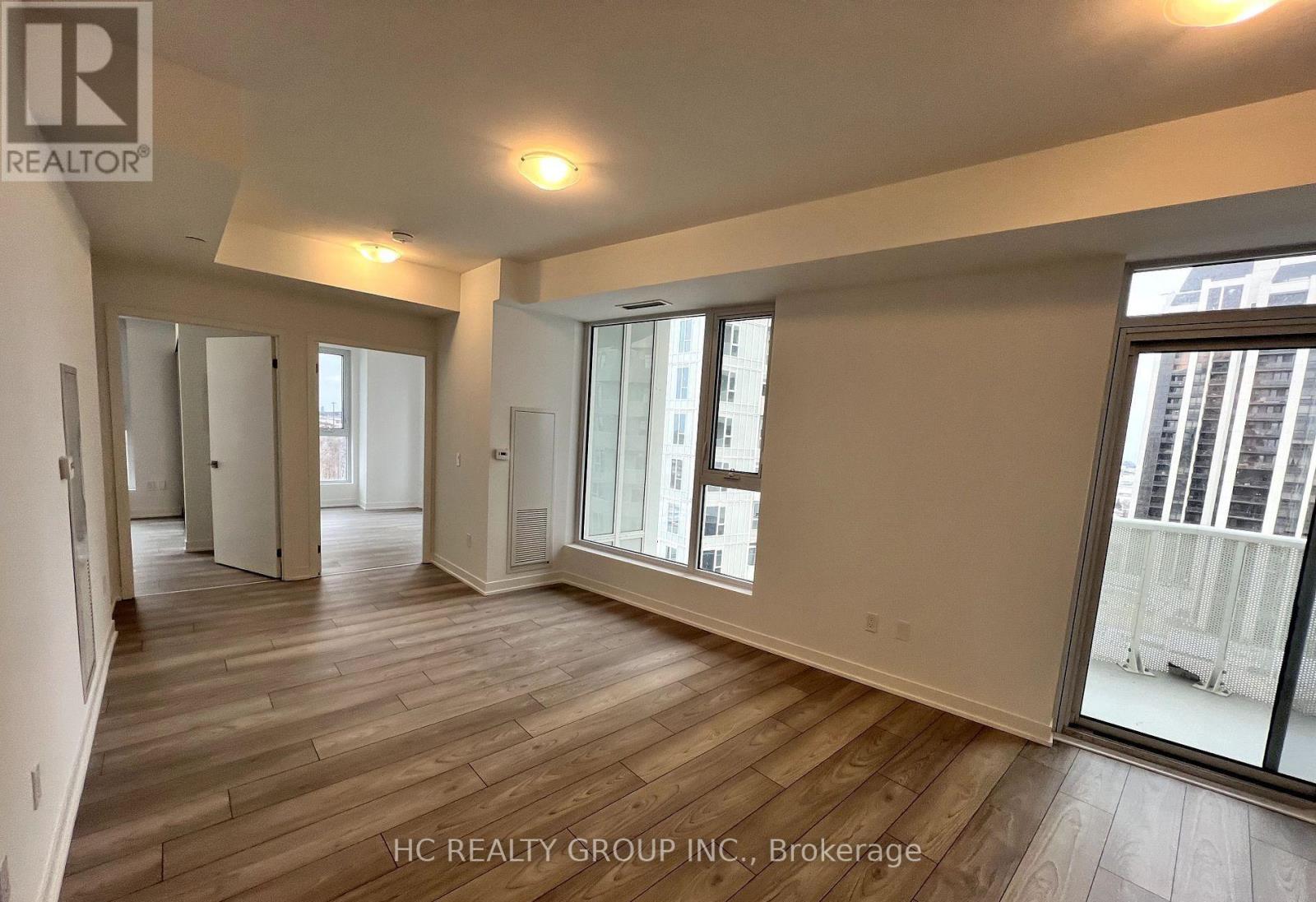 A spacious room with wooden flooring and large windows.